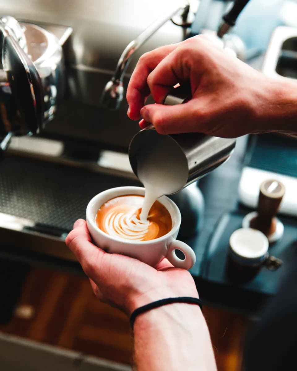 A barista pouring steamed milk into a coffee